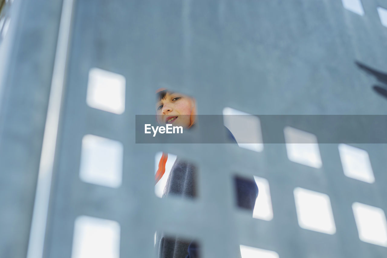 Low view of young boy through metallic fence while smiling to camera