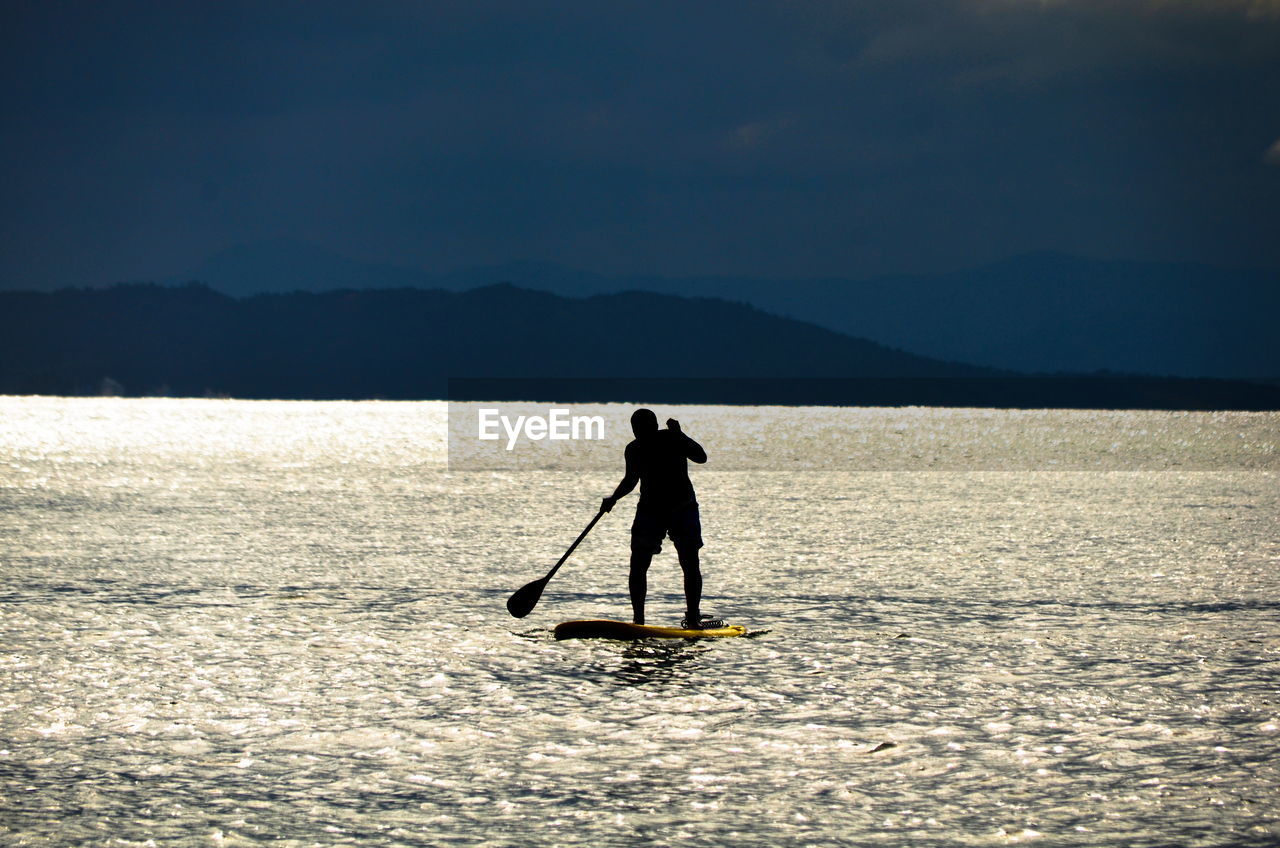 Silhouette man paddleboarding in lake