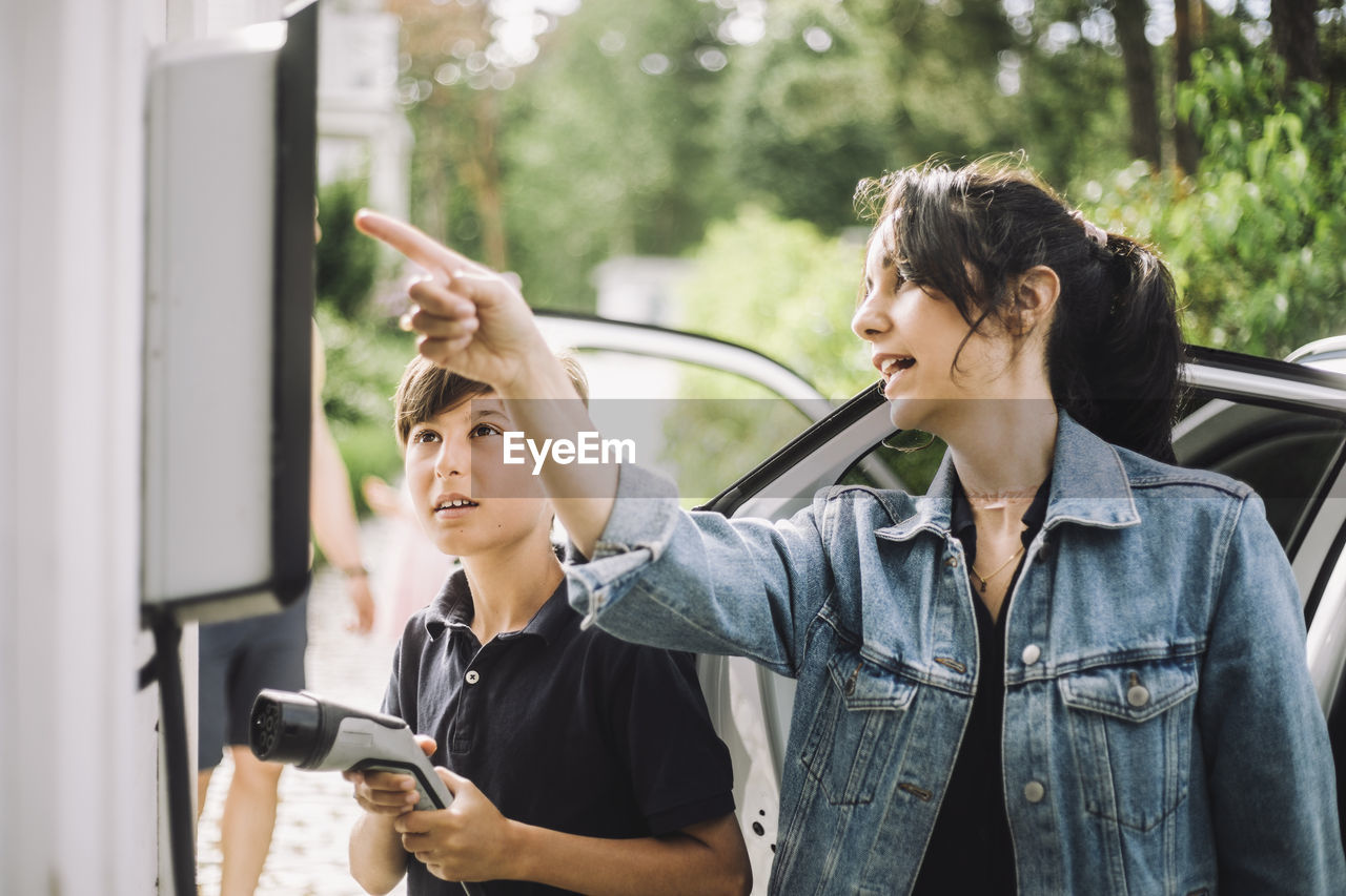 Mother pointing at charging board by son holding cable near car