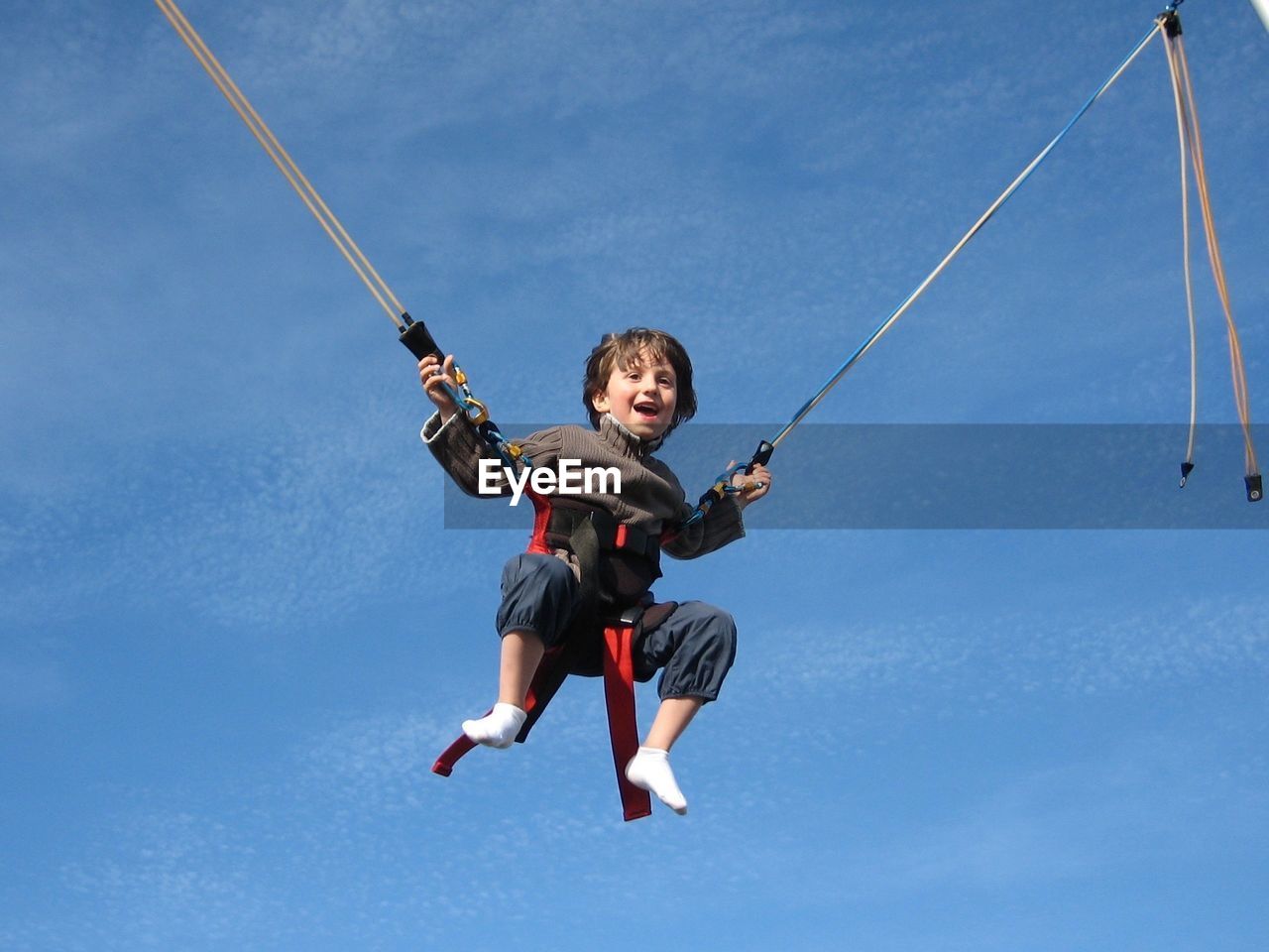 Low angle view of boy enjoying on bungee trampoline against blue sky