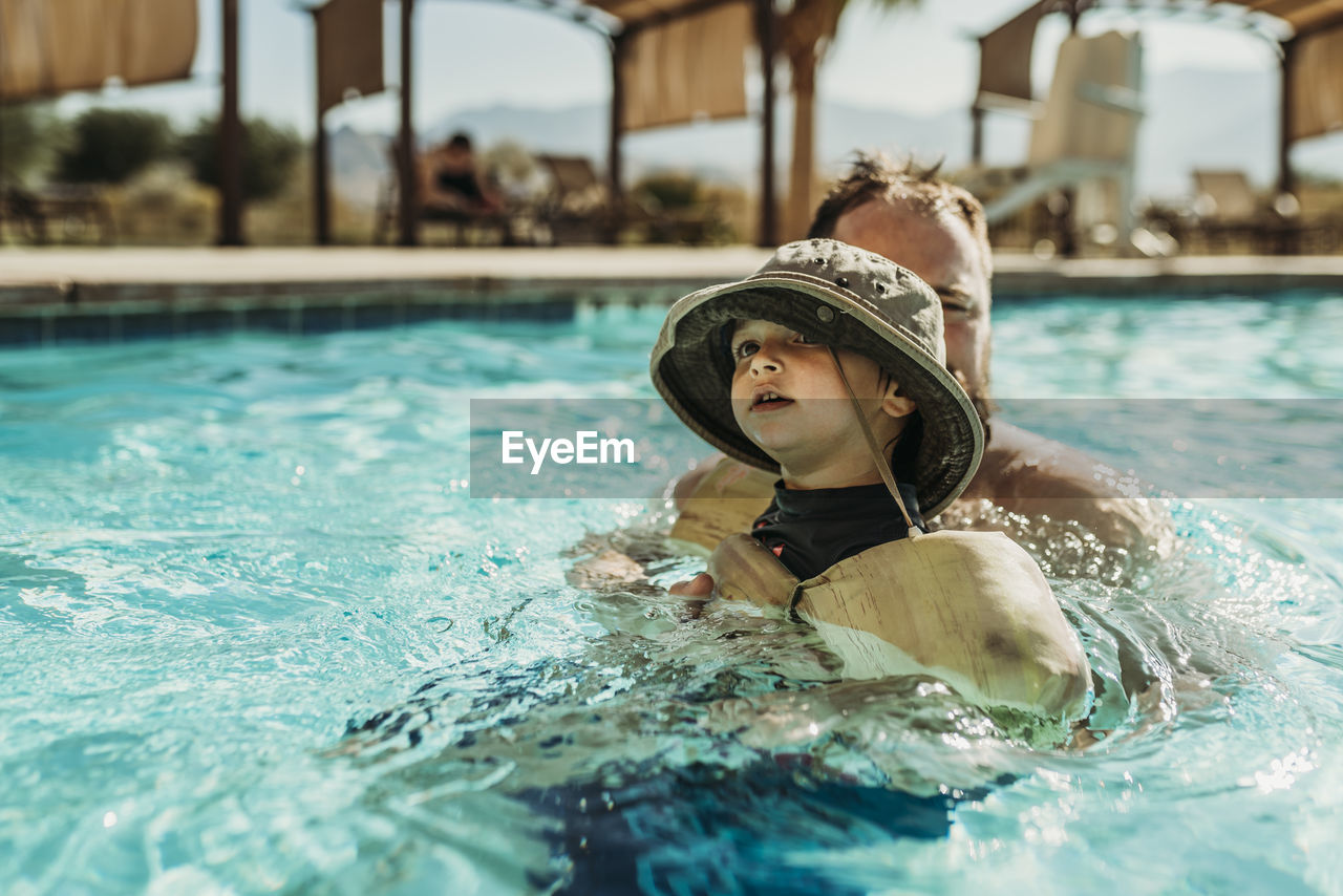 Close up of young toddler boy and father swimming in pool on vacation