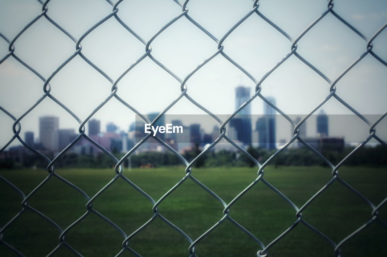 Close-up of buildings seen through chainlink fence against clear sky