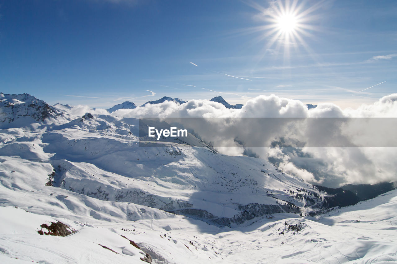 Ski resort la plagne in french alps - scenic view of snowcapped mountains above clouds with sunbeams