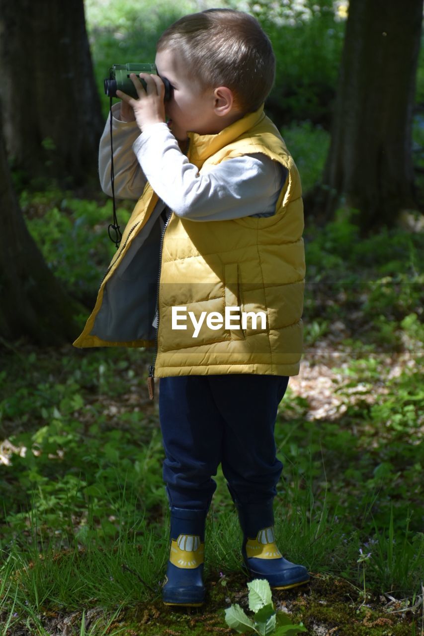 The boy looks through binoculars in the woods.