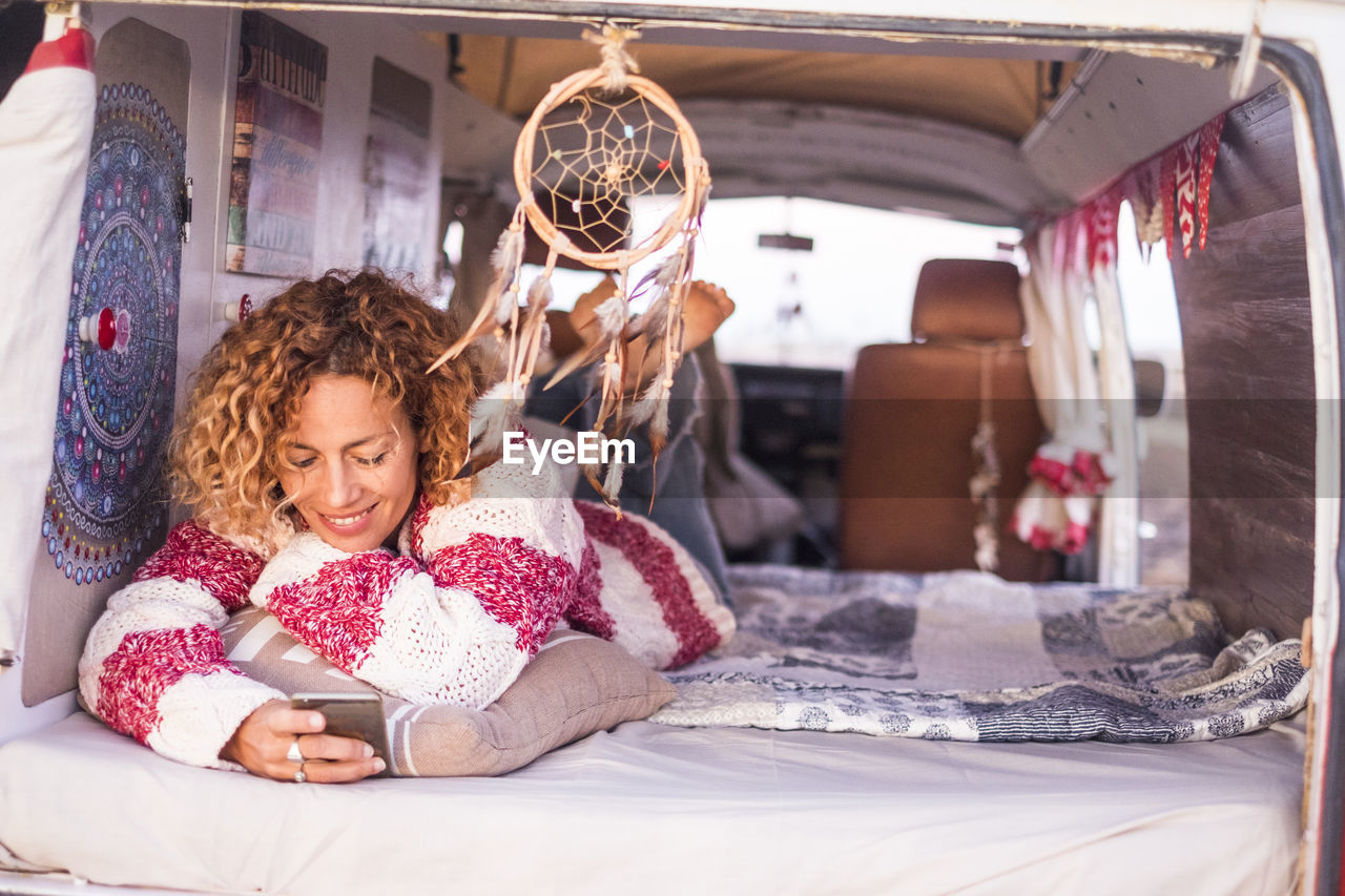 Smiling woman using mobile phone while lying by dreamcatcher hanging in vehicle