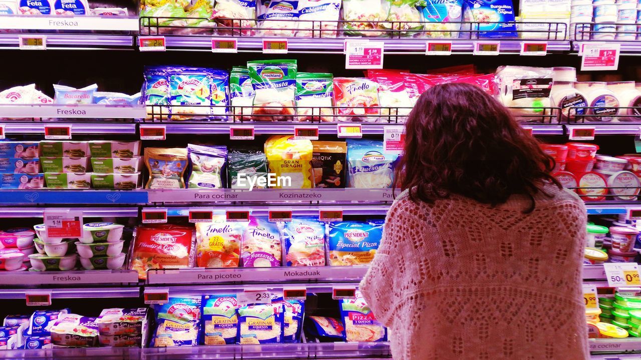 Rear view of woman standing by shelves in supermarket