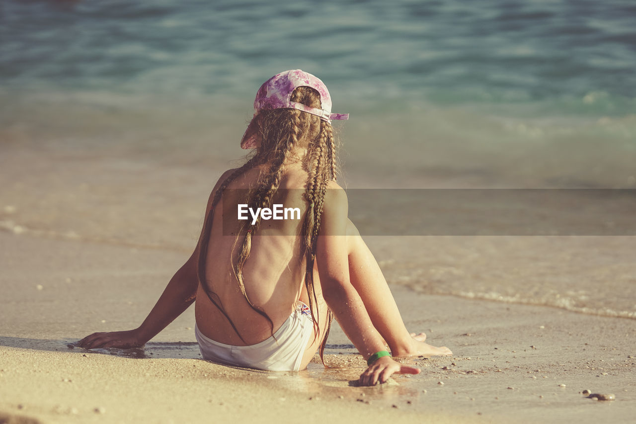 MIDSECTION OF WOMAN SITTING ON BEACH