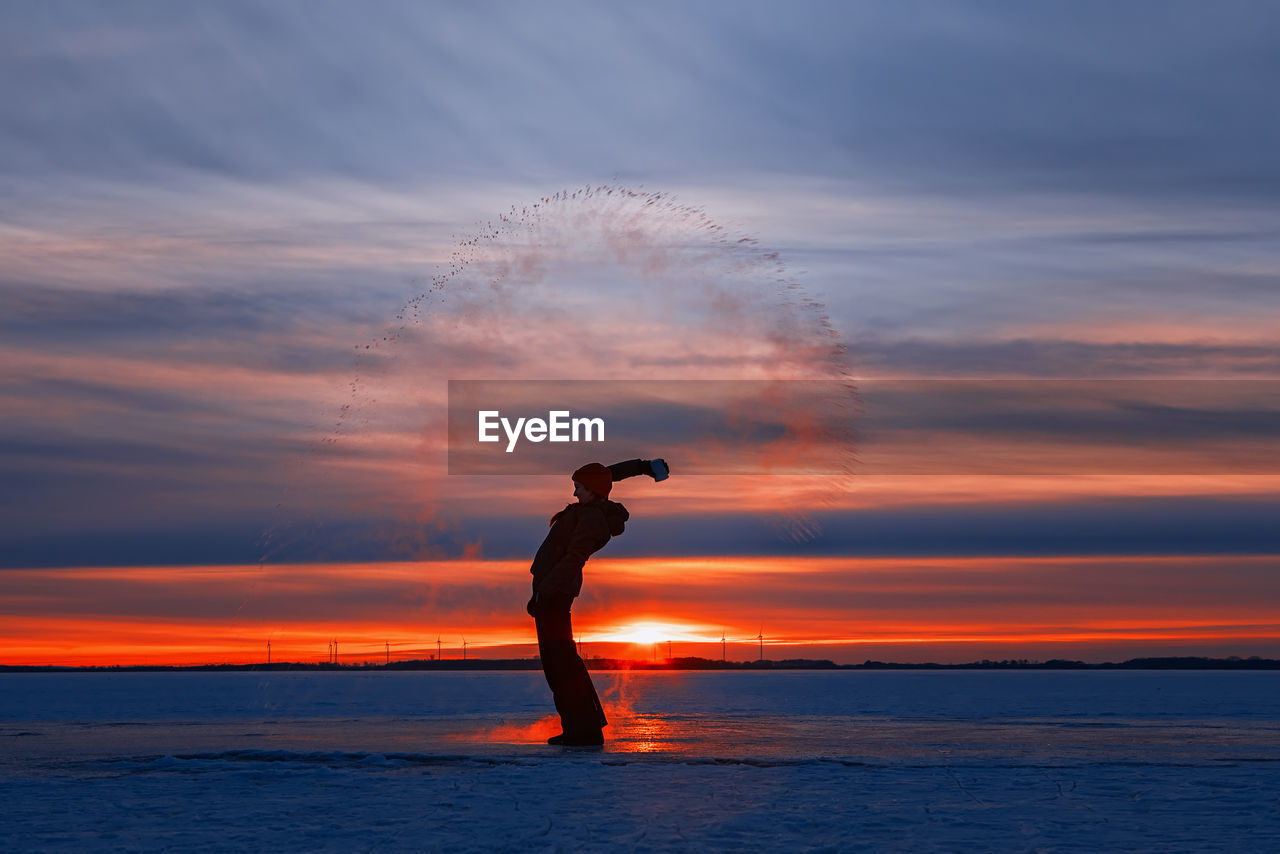 Silhouette man standing on beach against sky during sunset