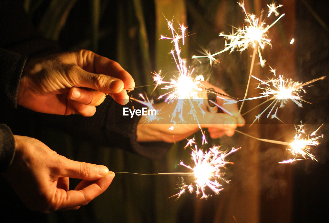 Close-up of people holding sparklers at night