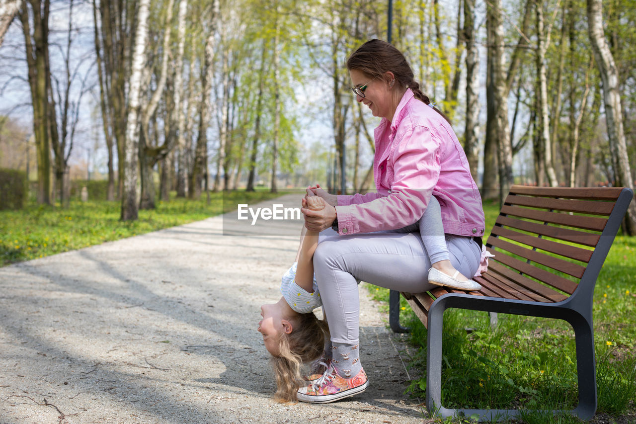 The daughter tilts her head completely down and the mother belays the little gymnast.