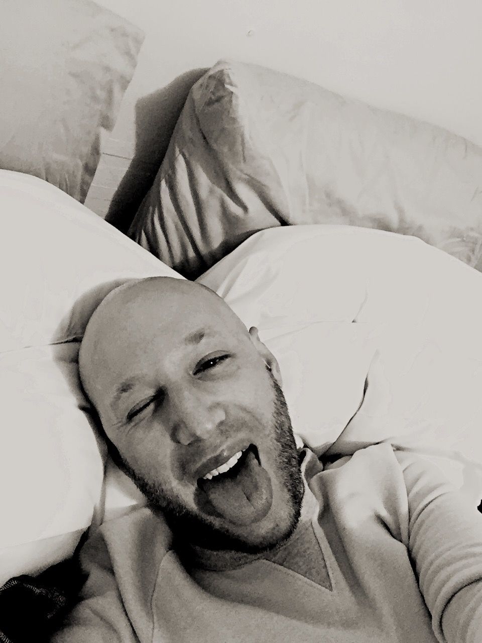 Portrait of man sticking out tongue while resting on bed at home