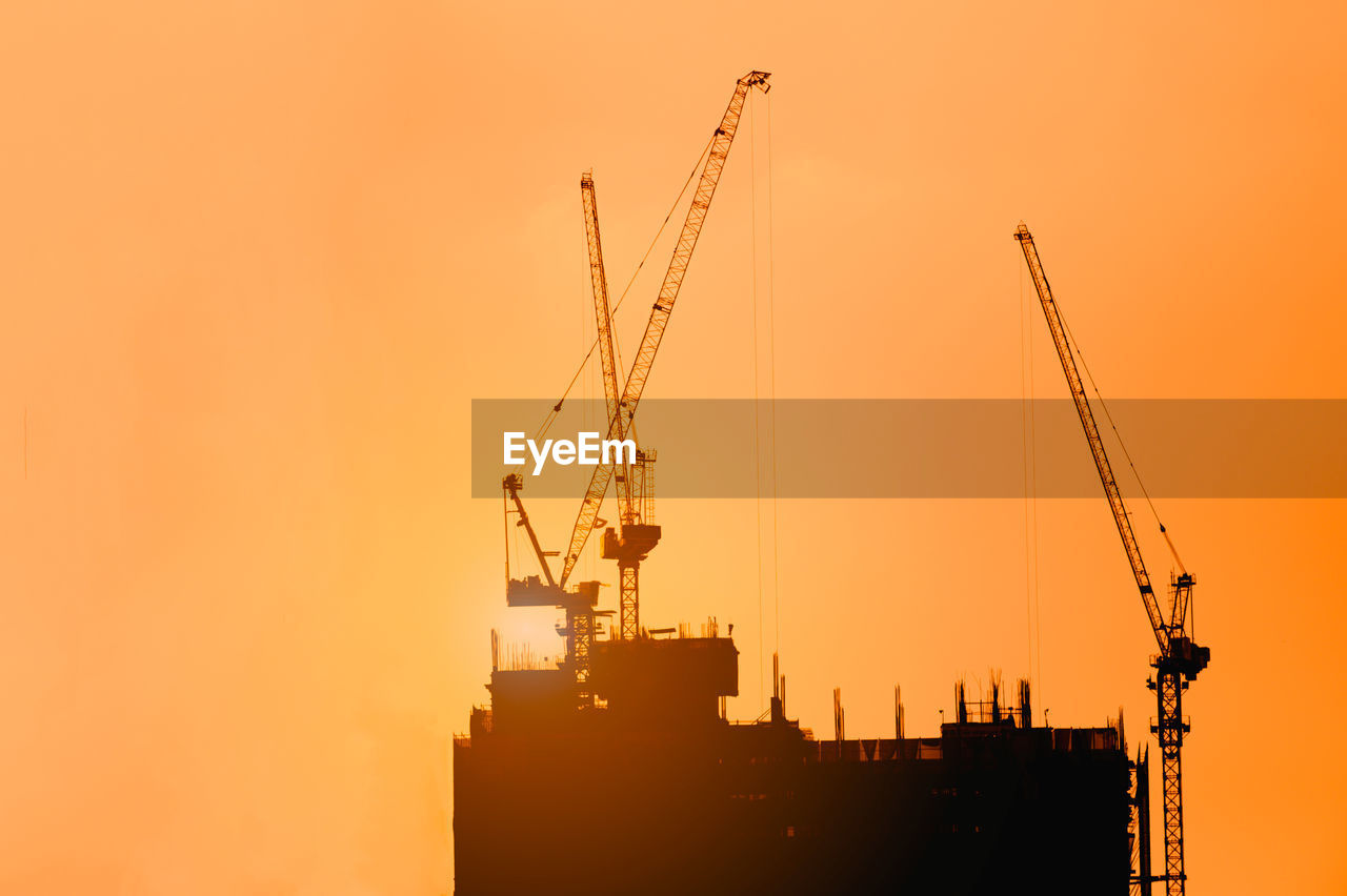 Cranes at construction site against clear sky during sunset