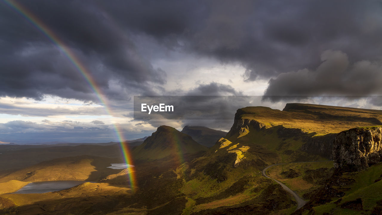 Scenic view of rainbow over mountain against cloudy sky