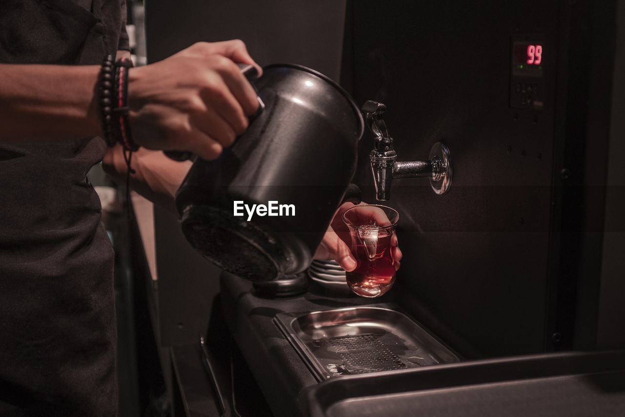 Midsection of man pouring water in coffee at darkroom