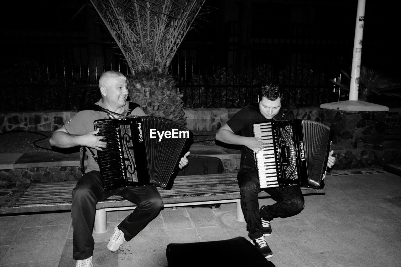 Full length of people playing accordion on bench at night