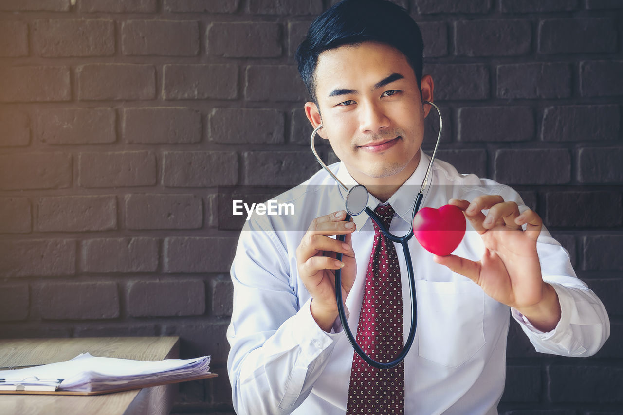 Portrait of smiling doctor holding model heart and stethoscope