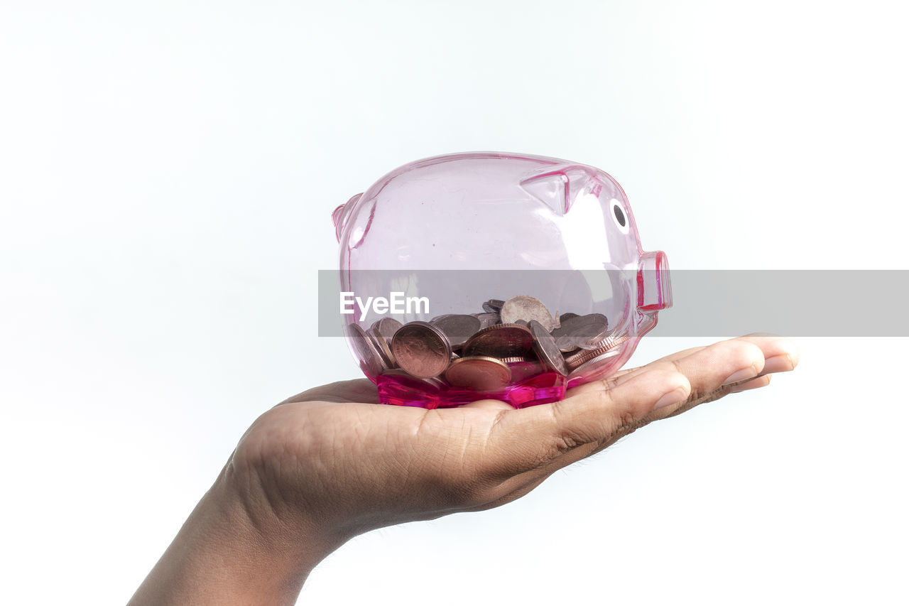 Cropped image of hand holding piggy bank against white background