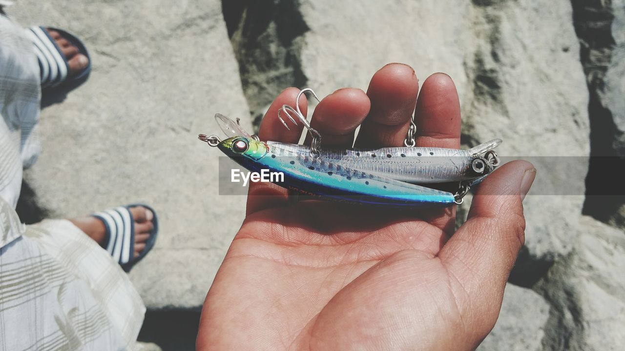 Copped hand holding fishing hooks at beach