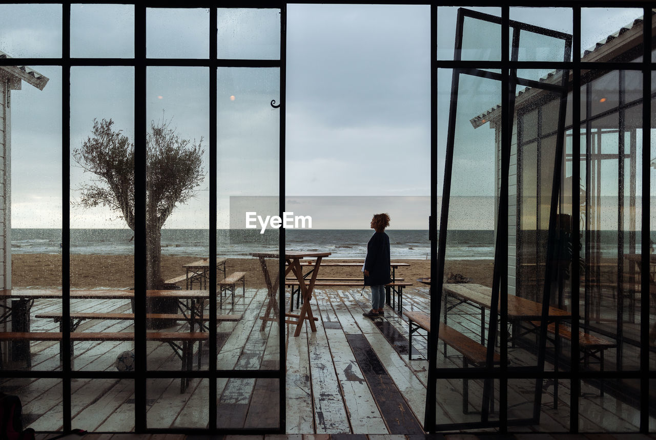 Rear view of woman standing outside of building and looking to the sea