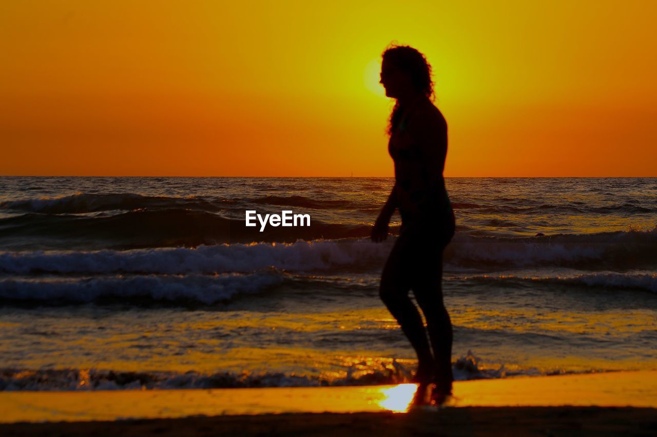 SILHOUETTE WOMAN STANDING ON BEACH DURING SUNSET