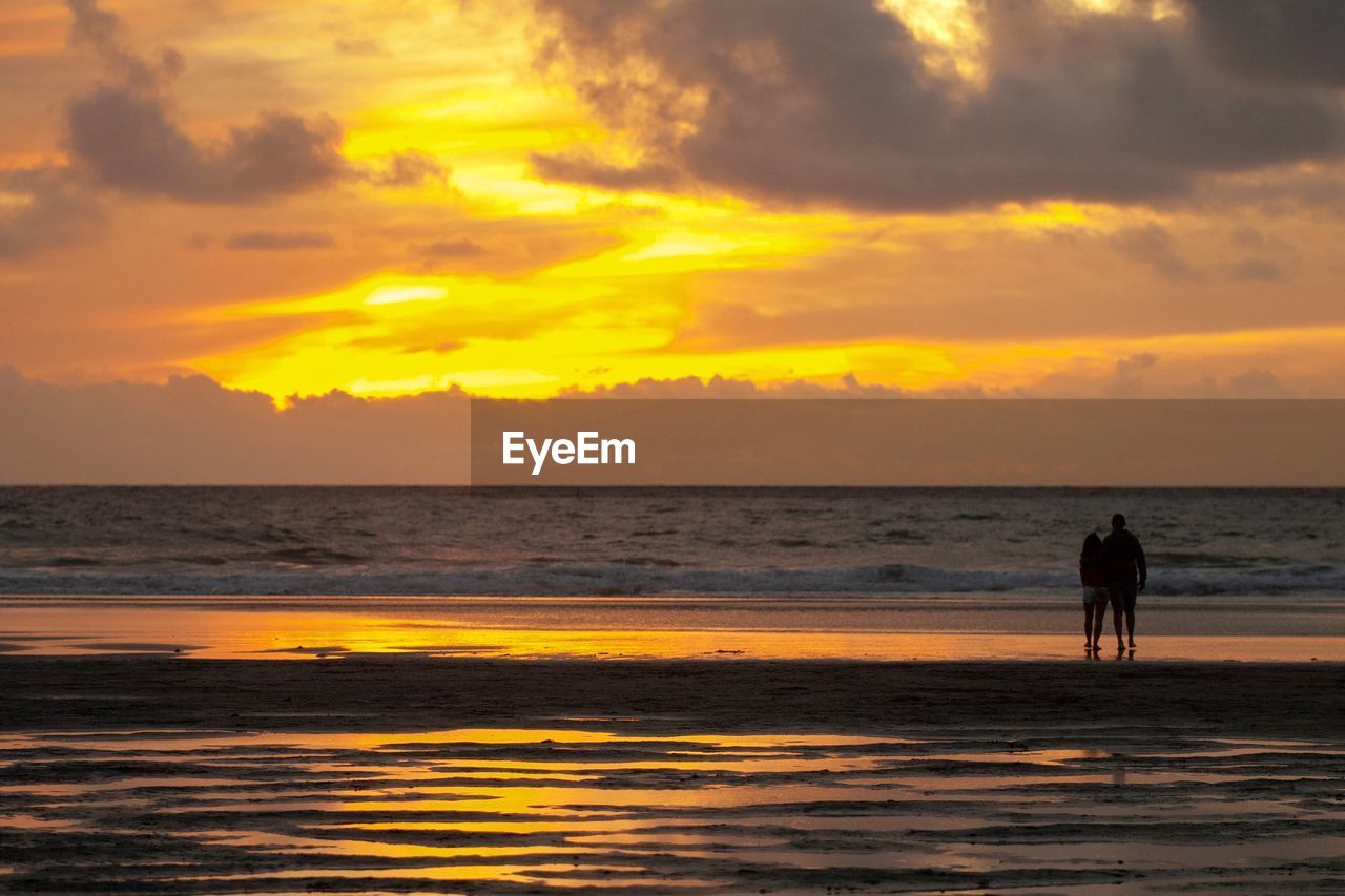 SILHOUETTE PEOPLE ON BEACH AGAINST ORANGE SKY