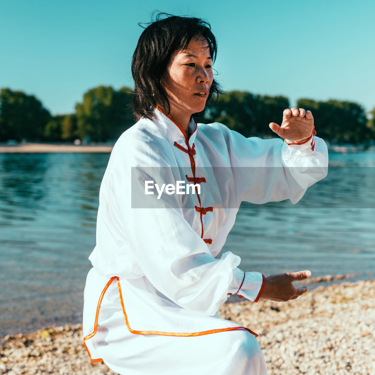 Woman practicing martial arts at lake against sky