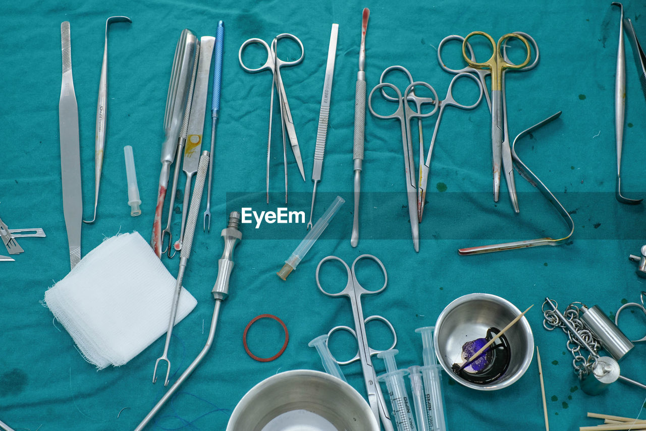 medical equipment, scissors, indoors, surgical equipment, no people, work tool, blue, large group of objects, healthcare and medicine, table, equipment, kitchen utensil, high angle view, medical, medical instrument, directly above, still life, metal, variation, household equipment, eating utensil, surgery, studio shot