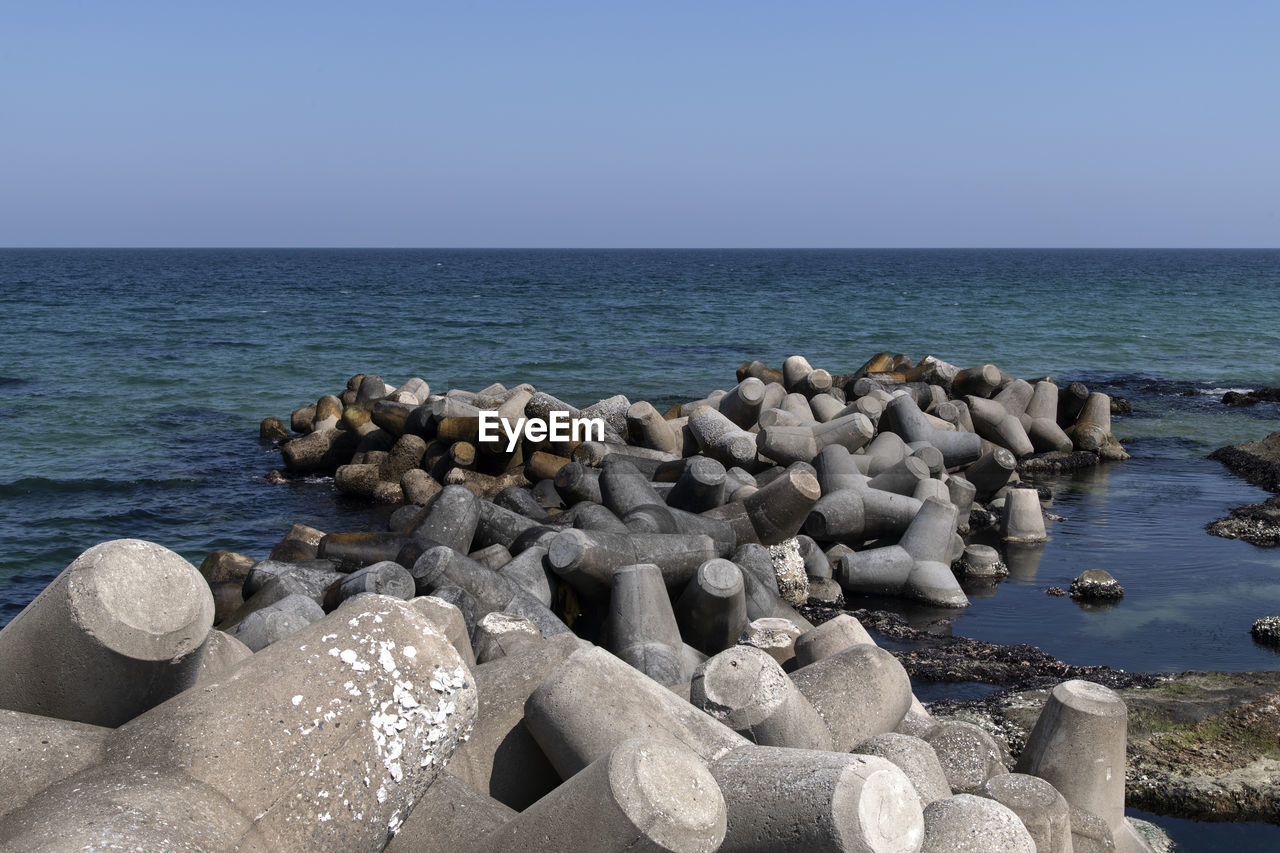 sea, water, rock, shore, horizon over water, sky, horizon, beach, land, nature, ocean, coast, beauty in nature, sand, scenics - nature, breakwater, tranquility, body of water, tranquil scene, clear sky, no people, day, stone, idyllic, outdoors, blue, non-urban scene, boulder, groyne, sunlight, sunny, travel destinations, wave, vacation, seascape