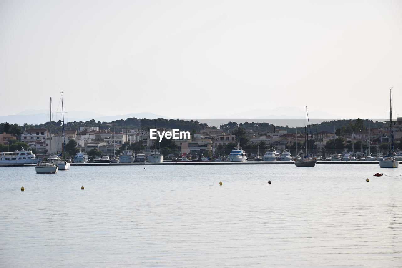 SAILBOATS IN RIVER BY BUILDINGS AGAINST SKY