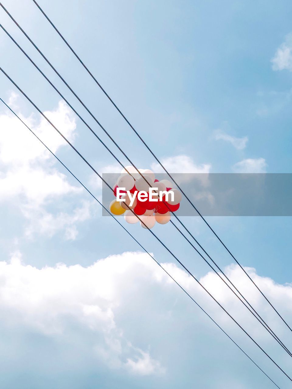 Low angle view of telephone pole against sky with balloons 