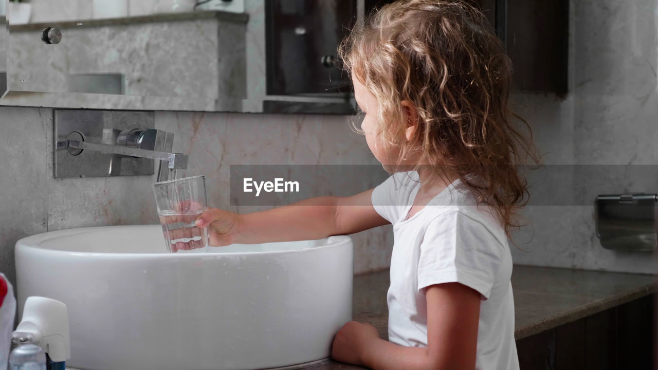Side view of girl filling water in glass at sink