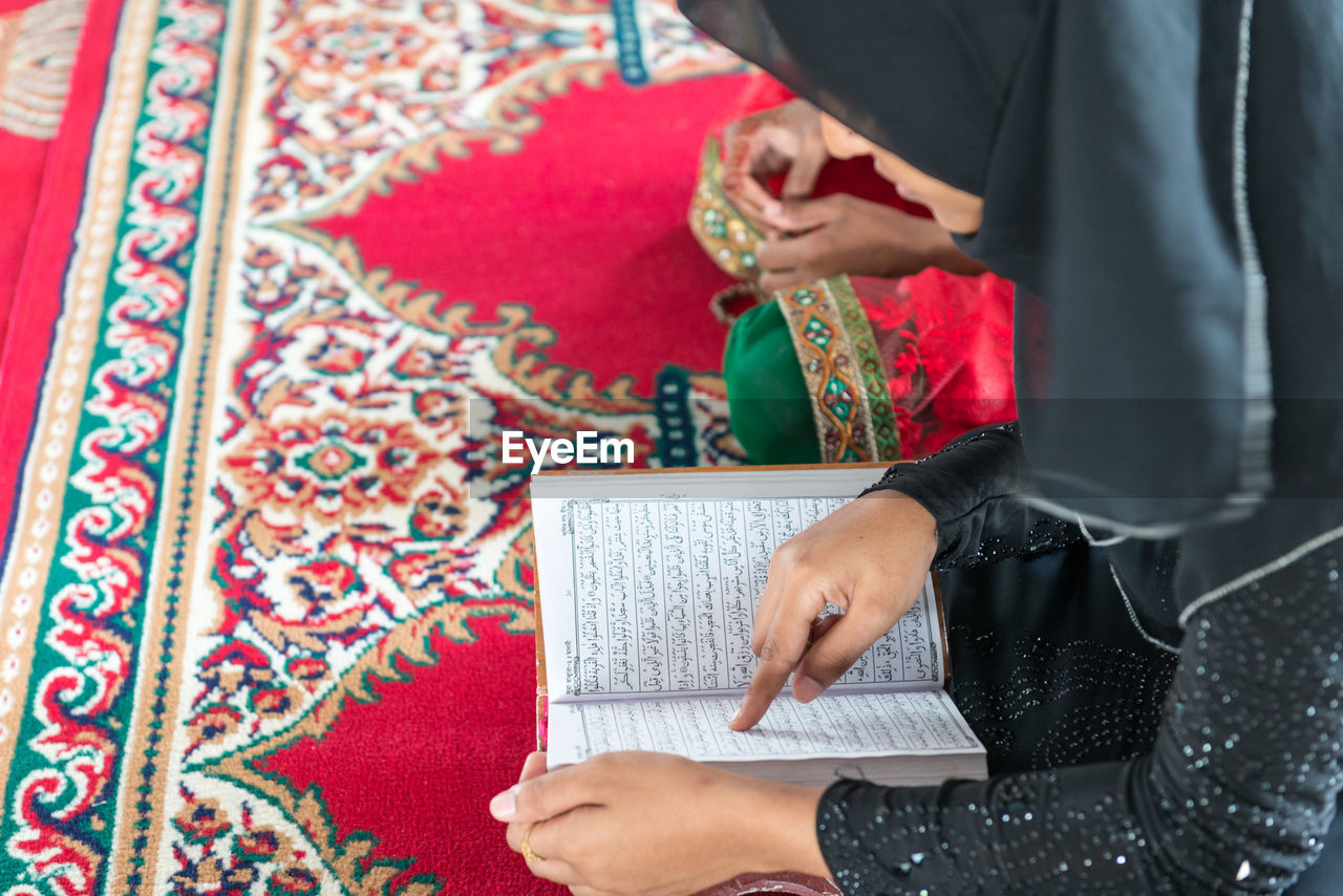 Woman reading koran while sitting on carpet