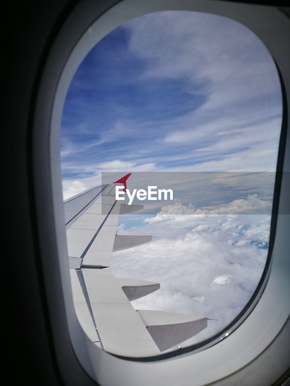 VIEW OF AIRPLANE FLYING OVER CLOUDS SEEN THROUGH WINDOW