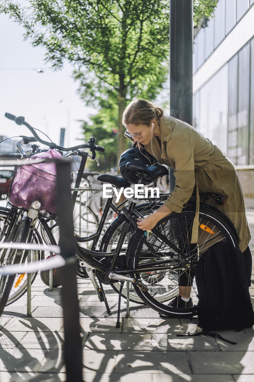 Businesswoman unlocking bicycle while standing at parking station