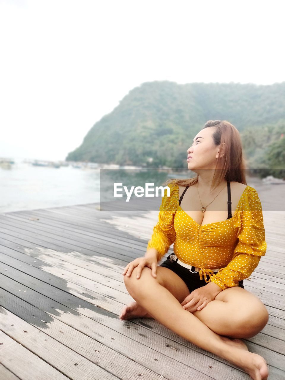 YOUNG WOMAN SITTING ON WOOD AGAINST MOUNTAINS