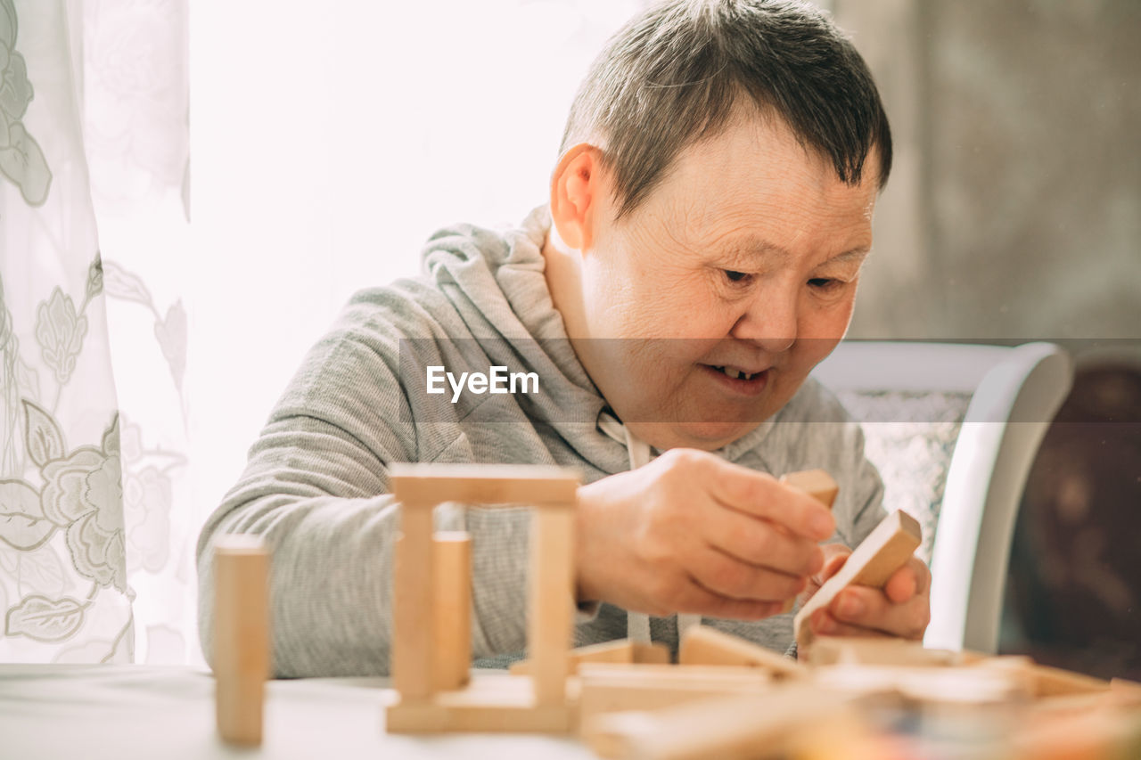 An elderly woman with down syndrome builds towers of their wooden toy blocks