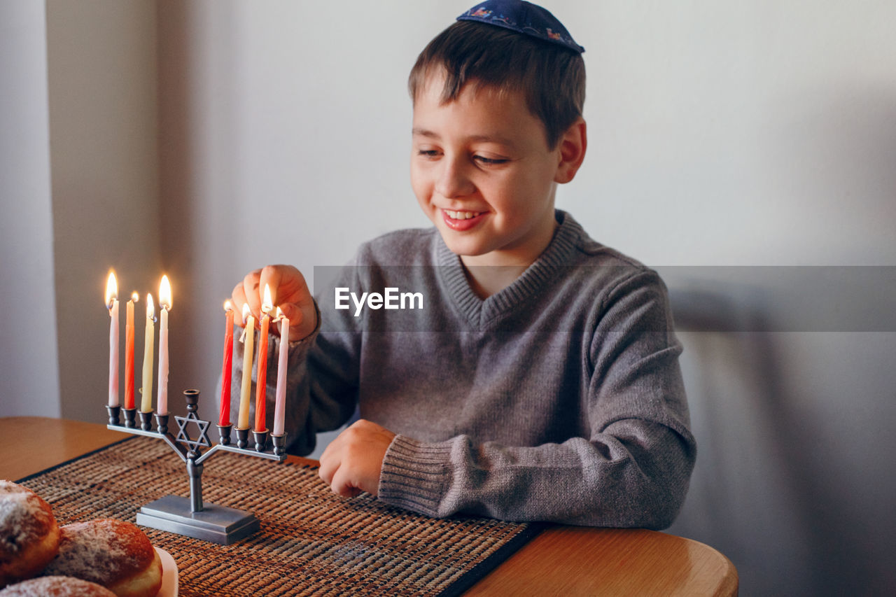 Boy in kippah lighting candles on a menorah for traditional winter jewish hanukkah holiday. 