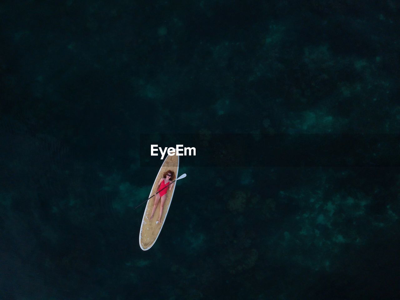 Aerial view of woman lying on paddleboard over sea