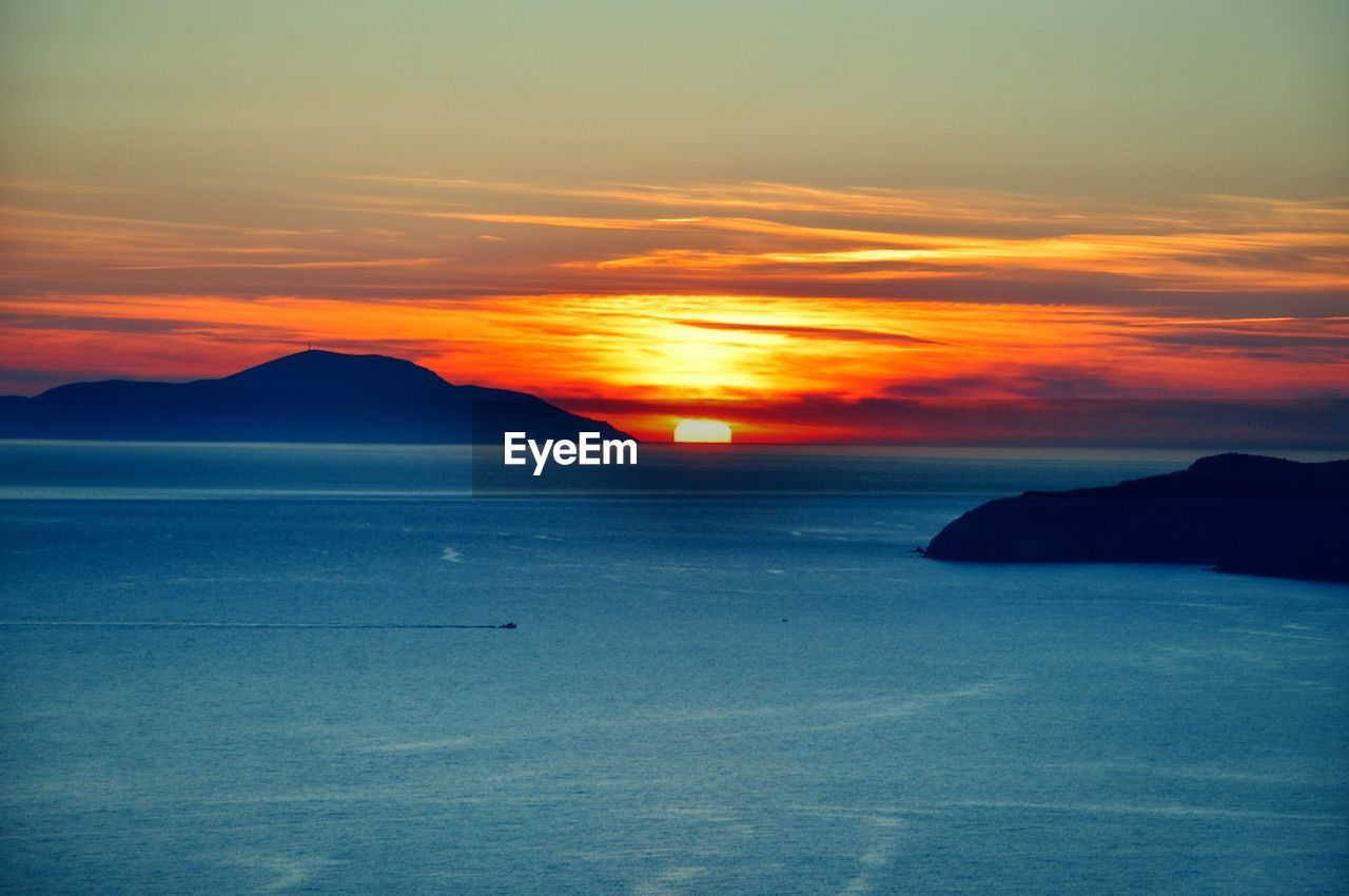 View of sea with silhouetted mountains at sunset