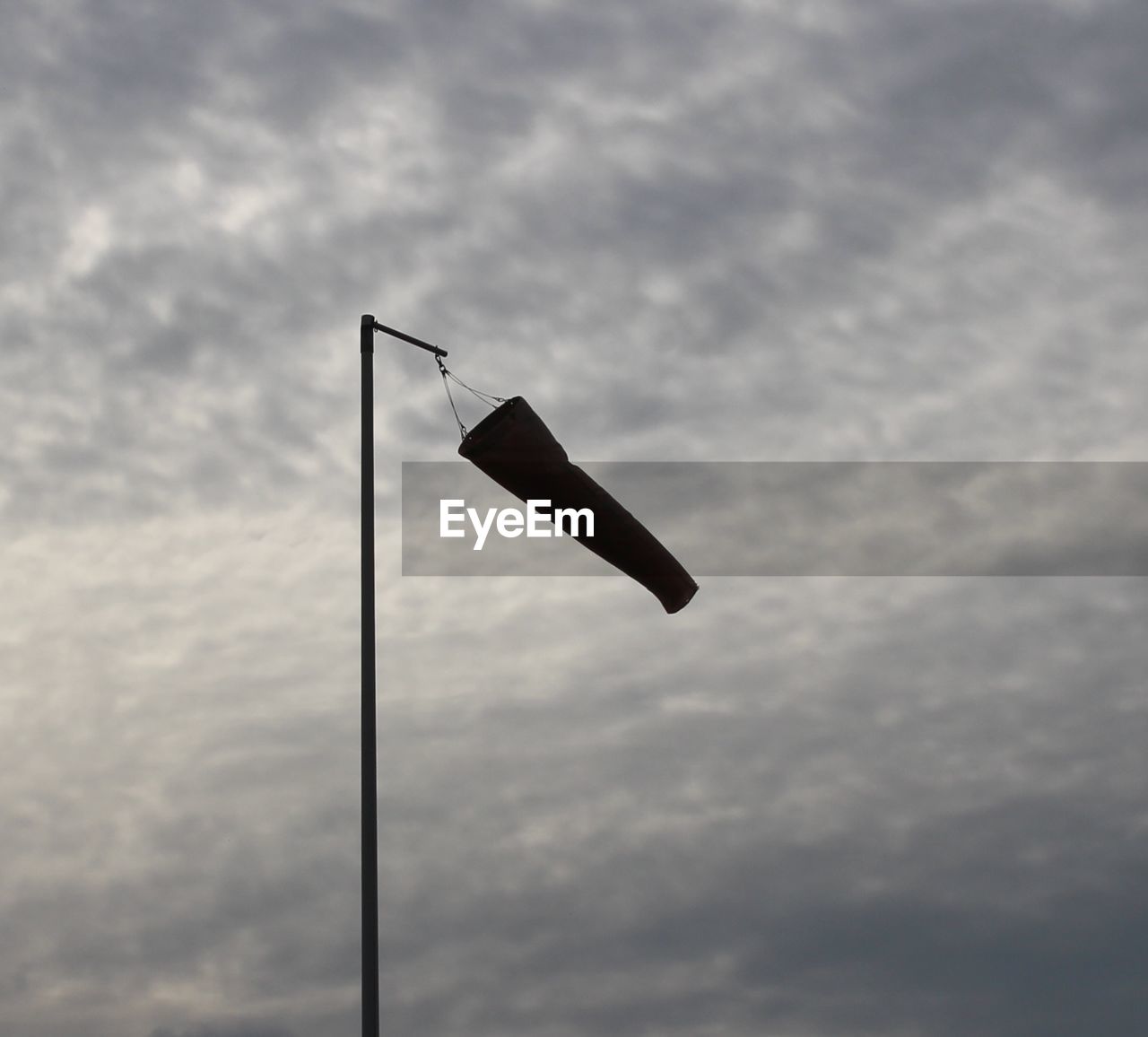 Low angle view of silhouette windsock against cloudy sky