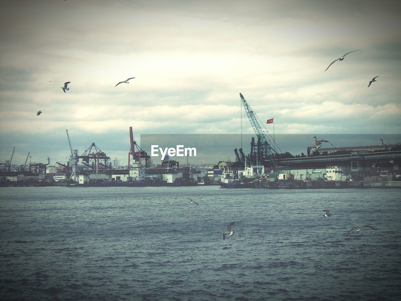 Cityscape by sea against cloudy sky