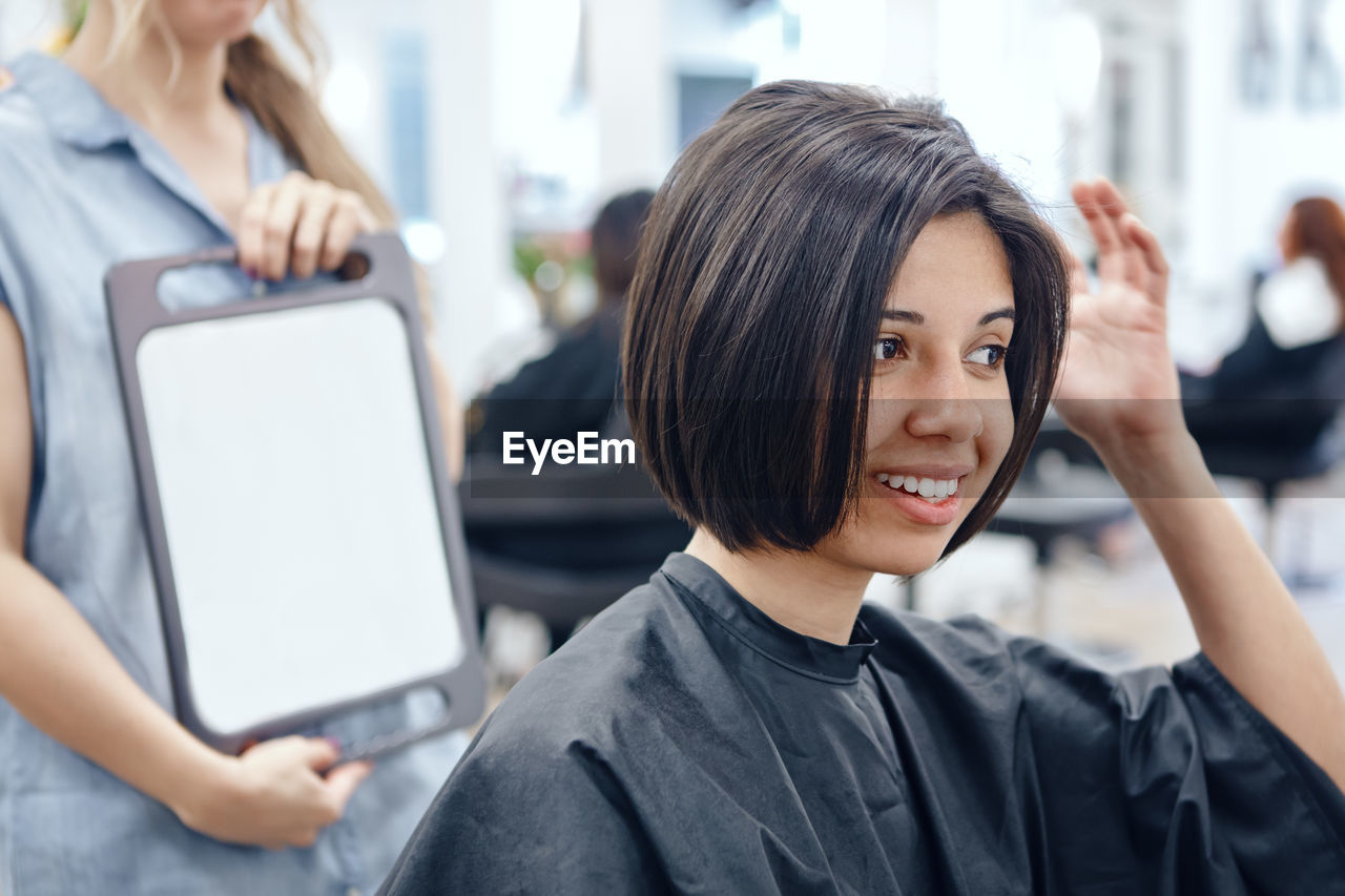 Beautician holding mirror for customer in salon