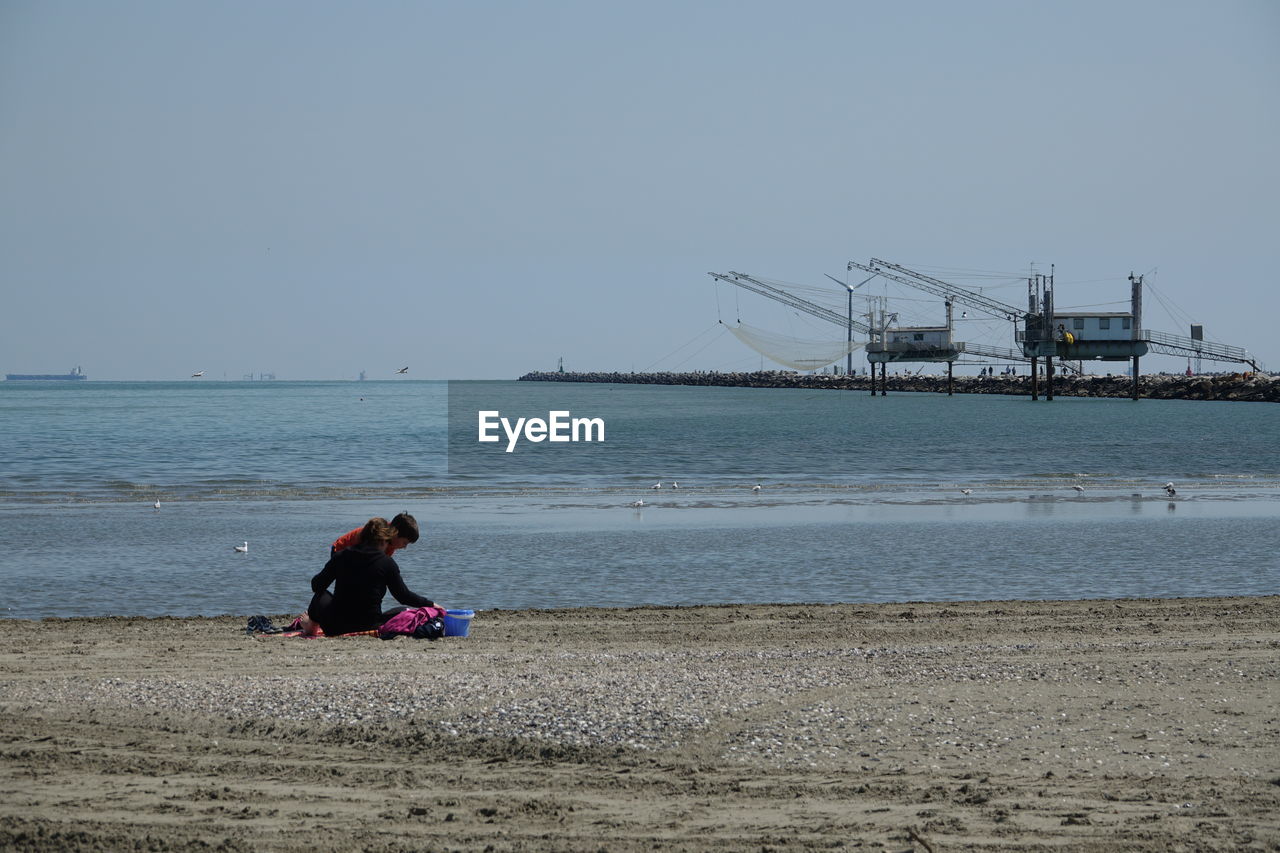 REAR VIEW OF WOMAN SITTING ON BEACH