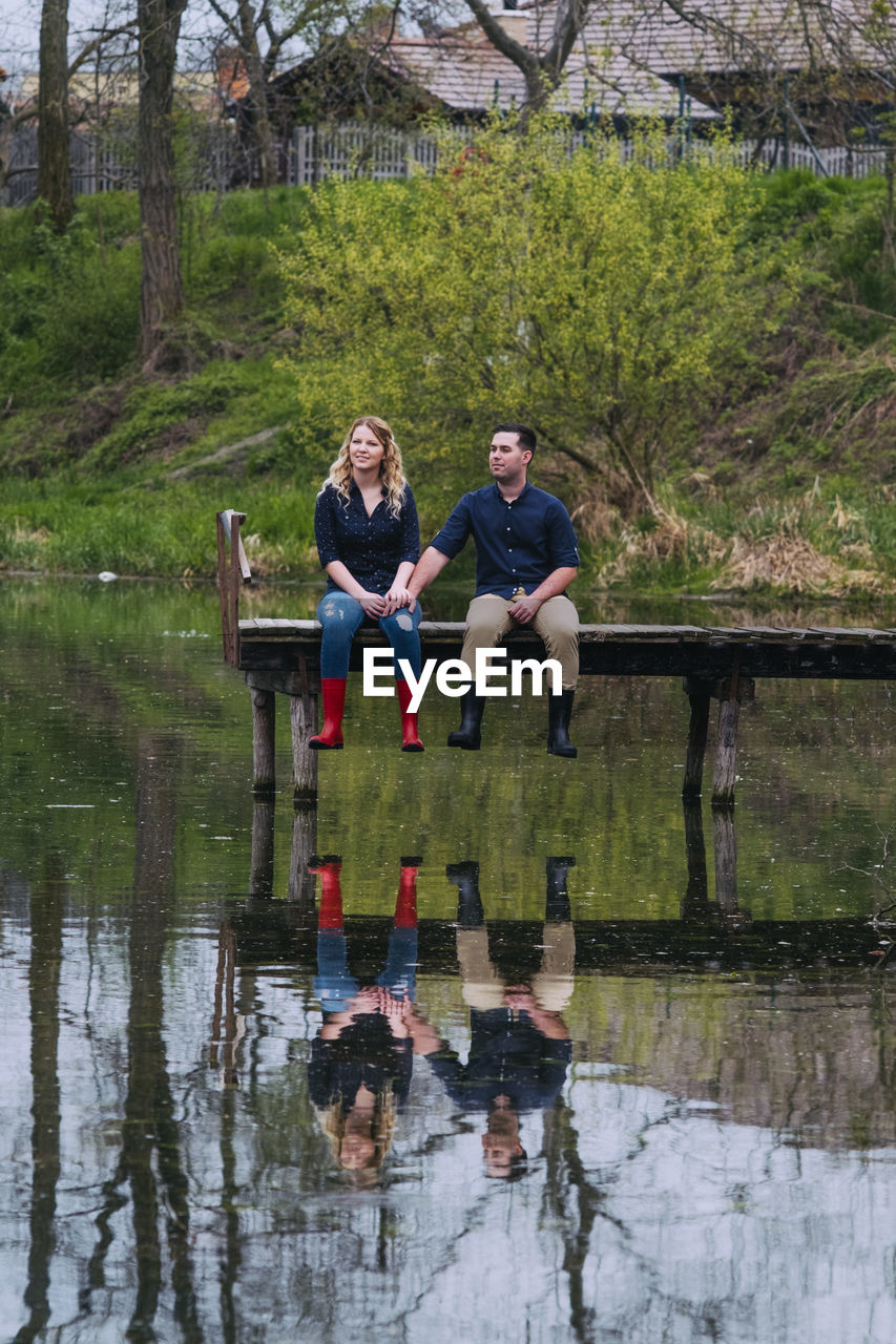 MEN SITTING ON FOOTBRIDGE OVER LAKE