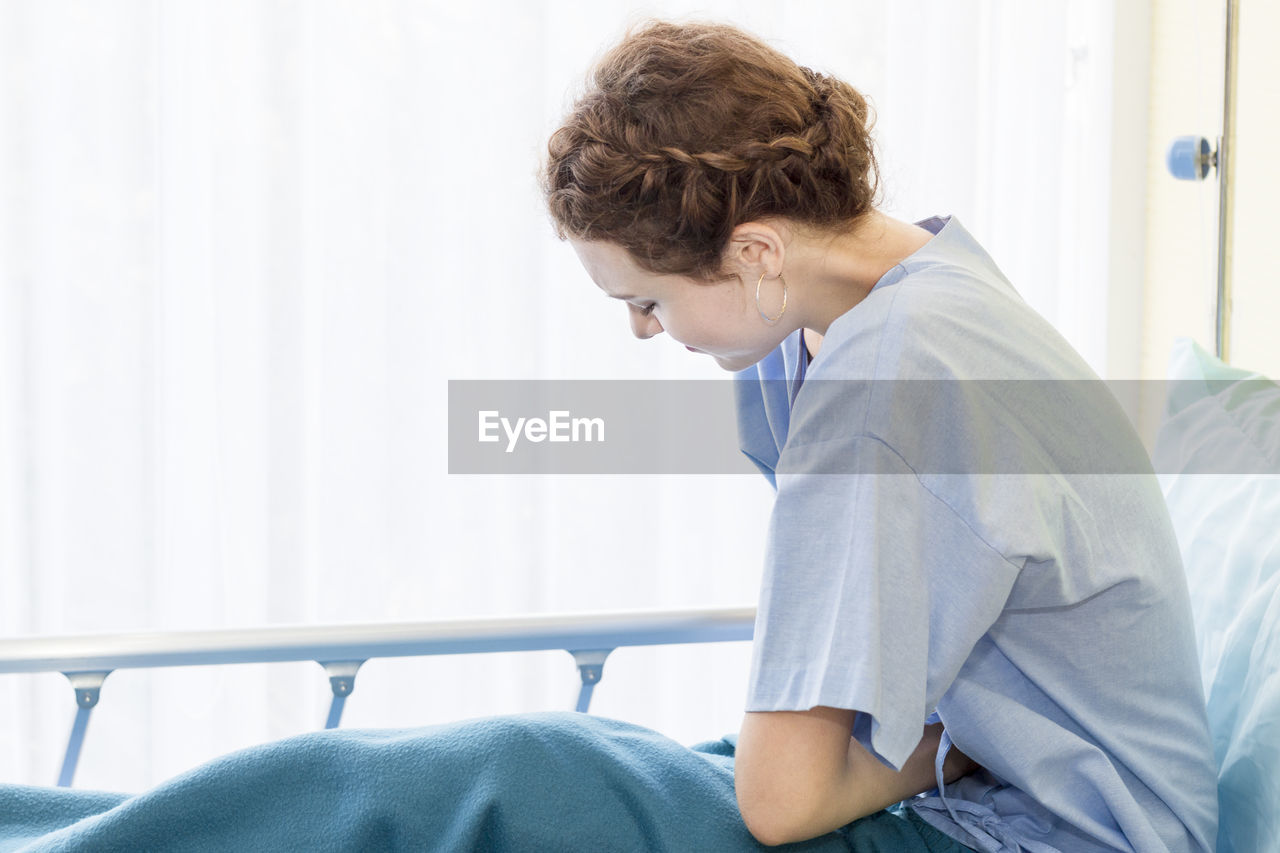 Young patient sitting on bed at hospital ward