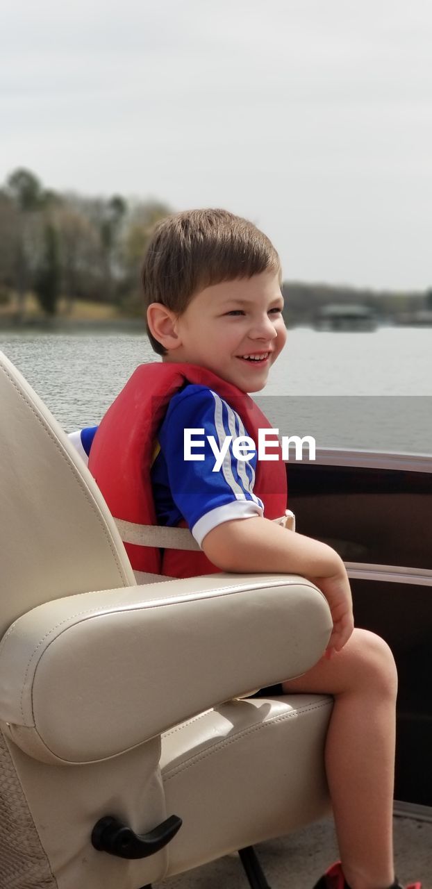 Boy smiling while sitting on boat in lake against sky