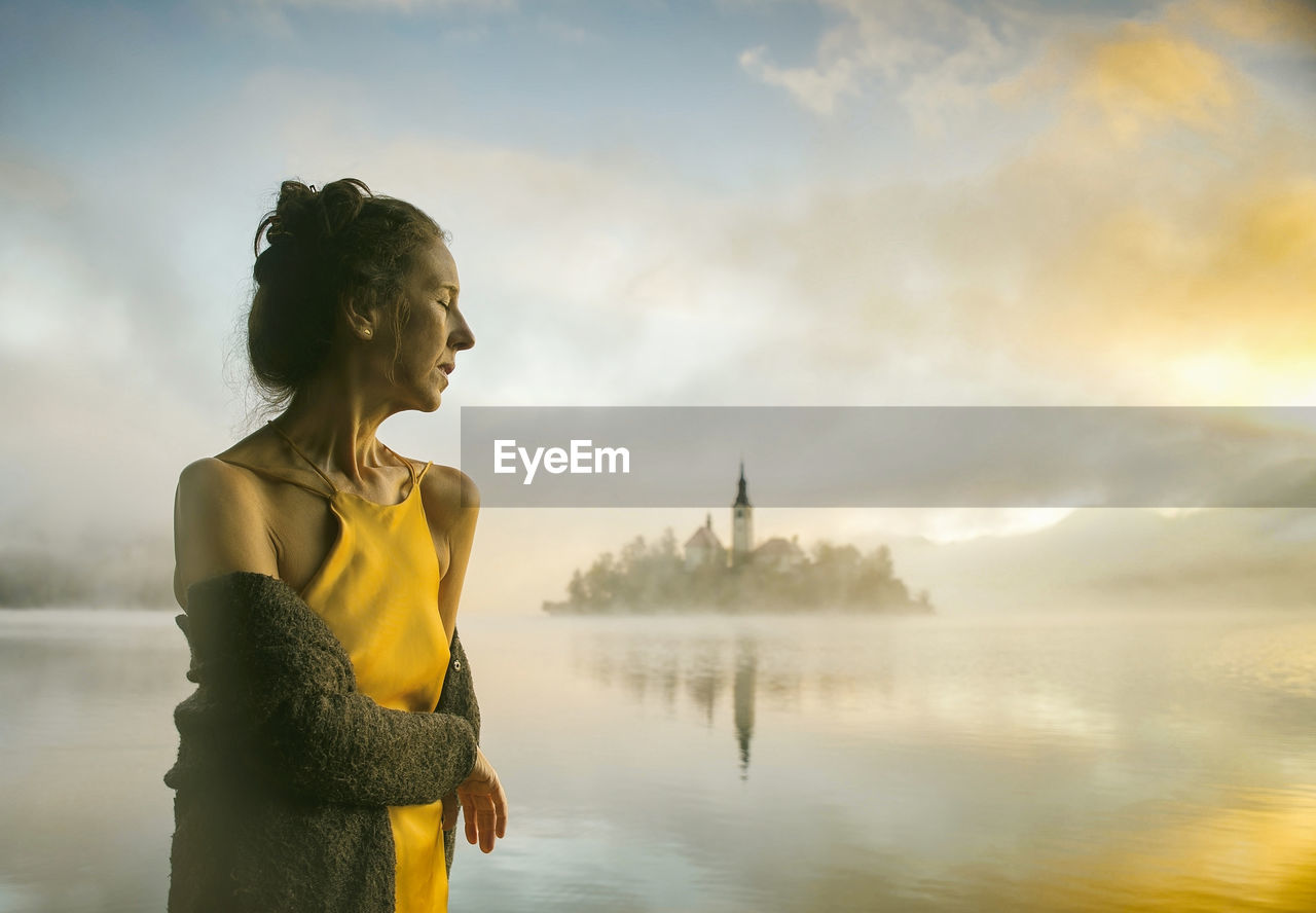 Woman in yellow dress watching a sunrise among the fog on the shores of lake bled, slovenia