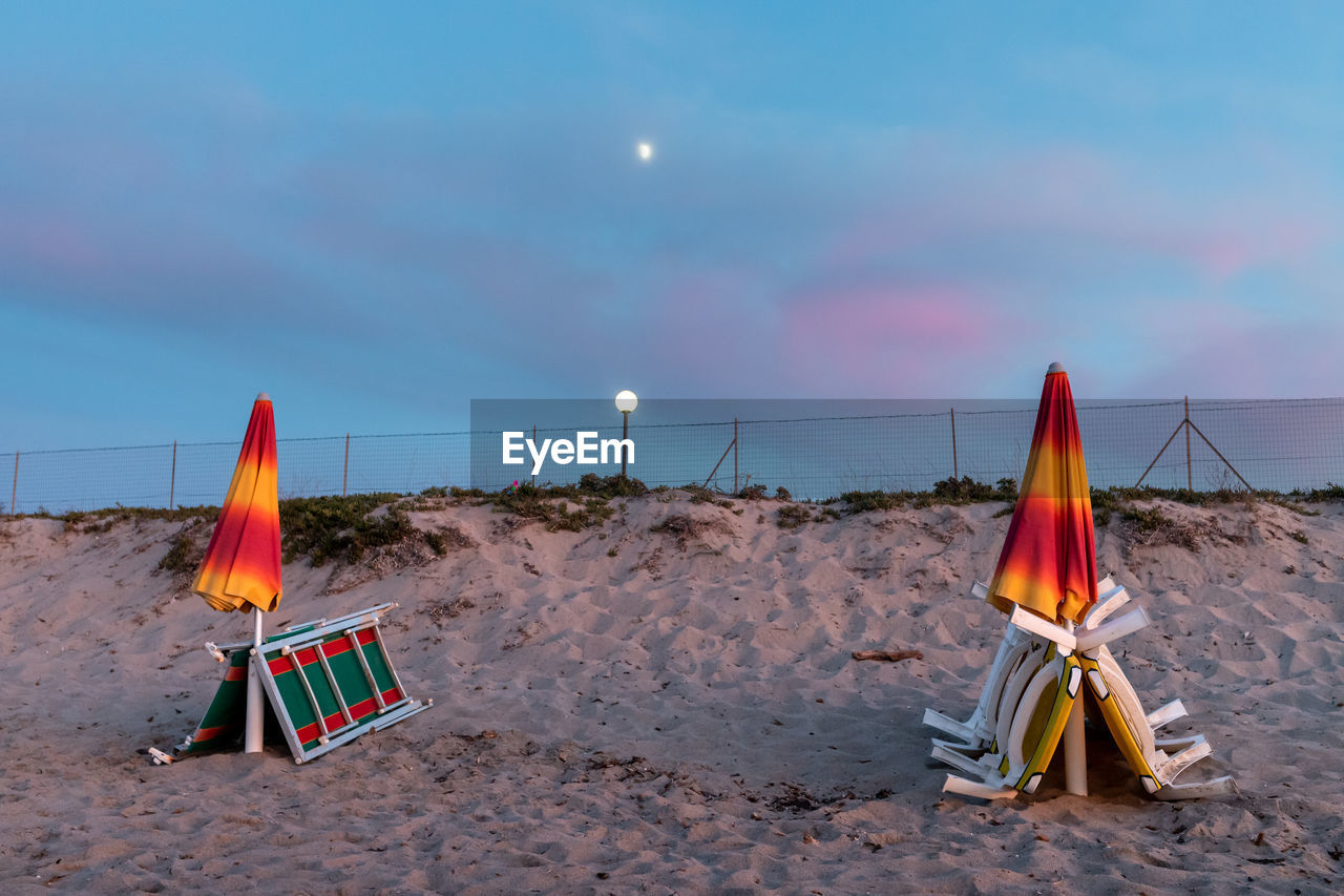 Chairs and umbrellas on beach against sky witho moonlight at blue hour