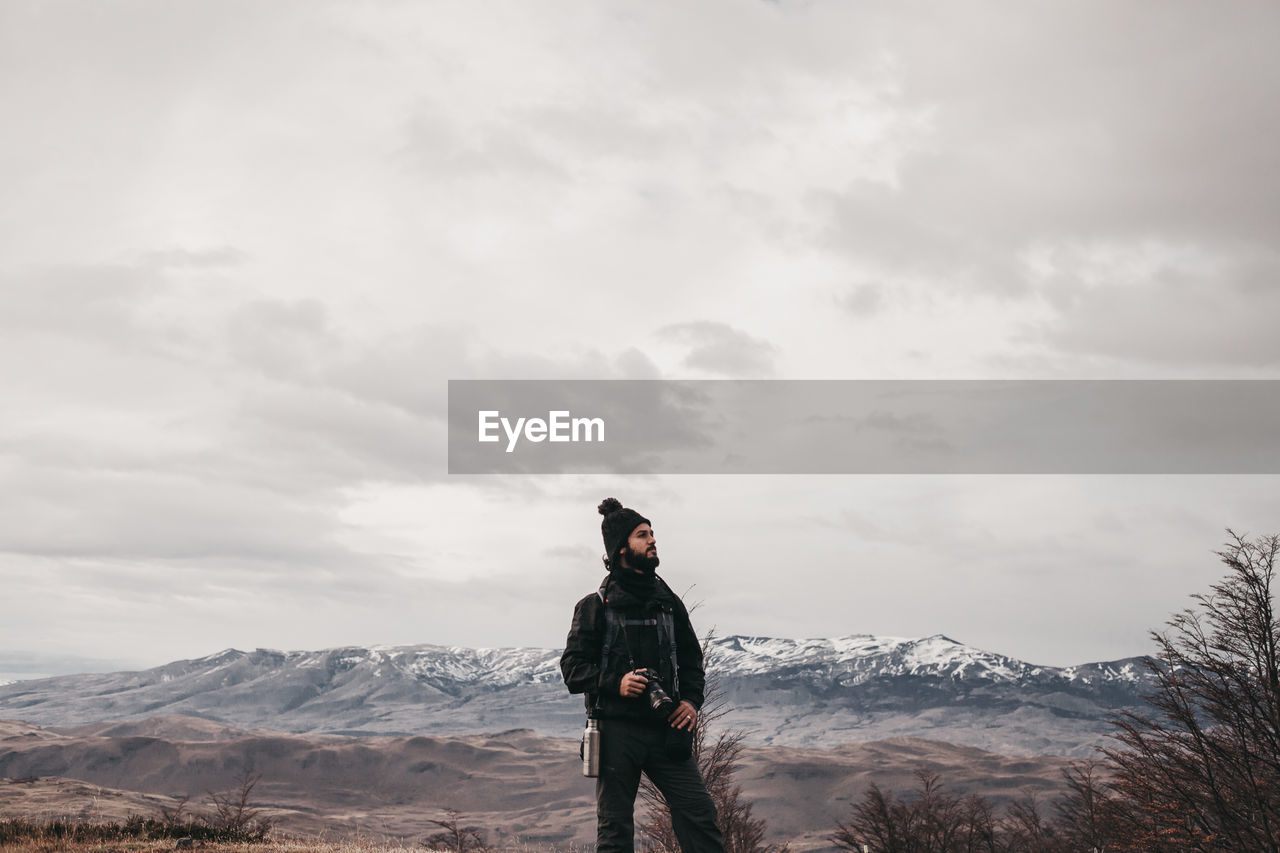 MAN STANDING ON MOUNTAINS AGAINST SKY