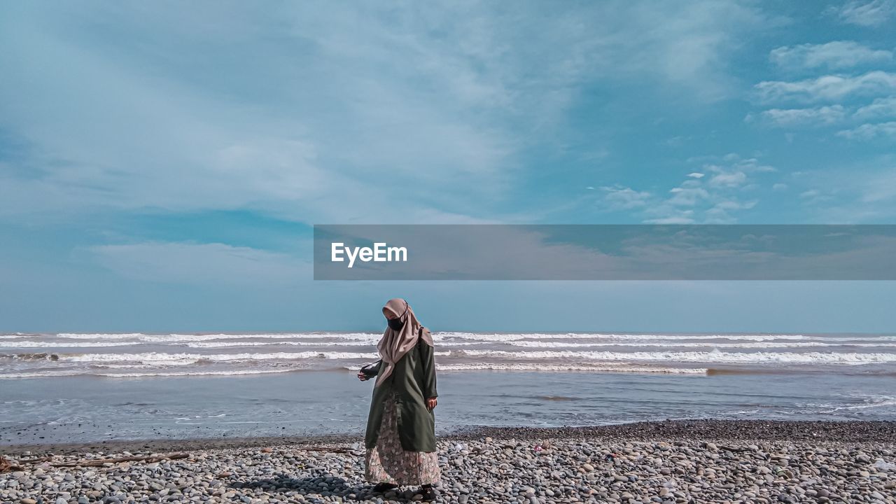 Full length of woman wearing mask on beach against sky